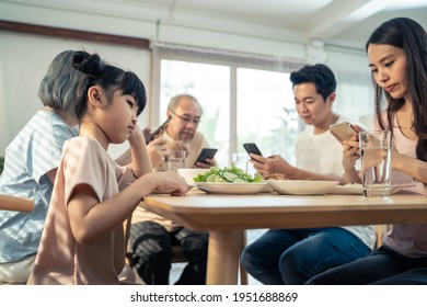 Upset Daughter Sitting At Lunch Table Looking To Addicted Parents And Grandparents Using Smartphones While Eating Breakfast. Ignoring Family Not Paying Attention On Small Child. Bad Parenting In House