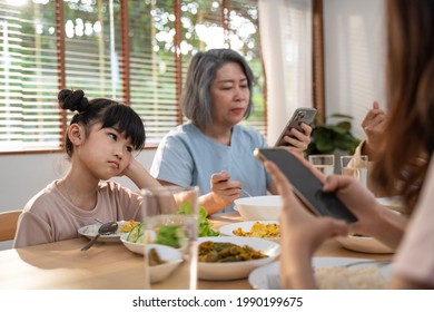 Upset Daughter Sitting At Lunch Table Looking To Addicted Parents And Grandparents Using Smartphones While Eating Breakfast. Ignoring Family Not Paying Attention On Small Child. Bad Parenting In House