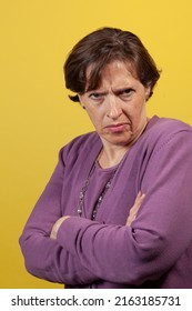 Upset defensive mature woman in purple blouse on a yellow background looking directly at the camera with arms folded scowling. - Shutterstock ID 2163185731