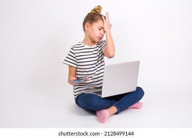 Upset Depressed Beautiful Caucasian Teen Girl Sitting With Laptop In Lotus Position On White Background Makes Face Palm As Forgot About Something Important Holds Mobile Phone Expresses Sorrow And Regr