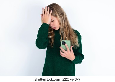 Upset Depressed Caucasian Teen Girl Wearing Green Knitted Sweater Over White Background  Makes Face Palm As Forgot About Something Important Holds Mobile Phone Expresses Sorrow And Regret Blames