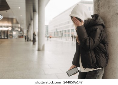 Upset and depressed girl holding smartphone and holding head. University sad student suffering from depression at high school. Lonely bullied teen. - Powered by Shutterstock