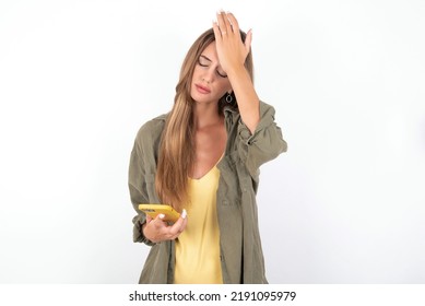 Upset Depressed Young Beautiful Woman Wearing Green Overshirt Over White Background Makes Face Palm As Forgot About Something Important Holds Mobile Phone Expresses Sorrow And Regret Blames