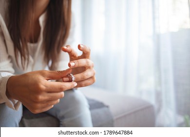 Upset depressed young woman holding wedding ring indoors, breaking off engagement, ending relationship, abandoned wife, cheated bride making hard decision, broken heart, breakup and divorce concept