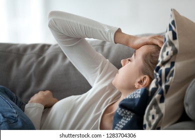 Upset depressed young woman lying on couch feeling strong headache migraine, sad tired drowsy teenager exhausted girl resting trying to sleep after nervous tension and stress, somnolence concept