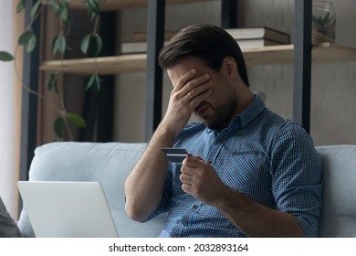 Upset desperate man having problems with wasting money, overspending,, scam and digital fraud. Frustrated disappointed shopaholic, bankrupt holding credit card at laptop, touching face