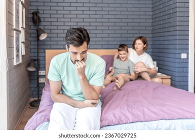 Upset and disappointed man sits on the edge of the bed and he cannot spend time with his wife because their son disturbs them - Shutterstock ID 2367029725