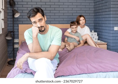 Upset and disappointed man sits on the edge of the bed and he cannot spend time with his wife because their son disturbs them - Shutterstock ID 2367029727