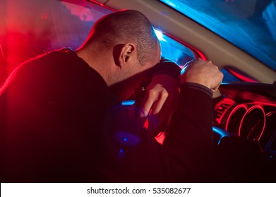 Upset drunk driver is caught driving under alcohol influence. Man covering his face from police car light.