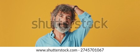 Upset elderly grey-haired bearded man wears blue shirt, looks at camera disappointed with result, isolated on orange background in studio. For banner. panoramic