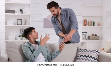 Upset father taking away phone from his son at home. Teenager problems - Shutterstock ID 2135395223