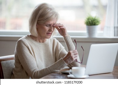 Upset fatigued overworked senior mature business woman taking off glasses tired of computer work, exhausted middle aged employee suffers from blurry vision after long laptop use, eye strain problem