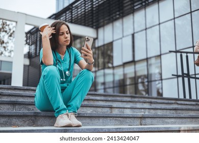 Upset female nurse. Medical professional looking unhappy. Shot of a young nurse looking stressed out while sitting at stairs in a hospital. Upset female nurse - Powered by Shutterstock