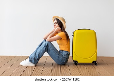 Upset Female Tourist Sitting Near Suitcase And Looking Away At Free Space Over Light Wall Background. Female Traveling Abroad To Travel On Weekends Getaway. Air Flight Journey Concept