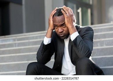 Upset and fired office worker sitting on stairs outside office building close up businessman in business suit depressed lost money bankrupt african american worker sitting sad. - Powered by Shutterstock