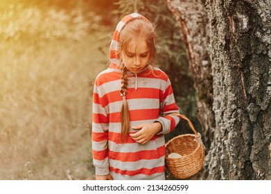 Upset Or Focused Eight Year Old Kid Girl Mushroom Picker Is Seek For And Picking Mushrooms In The Forest. Child Survivalists Gathers A Wild Fungus Harvest And Outdoor Foraging  In Nature. Flare