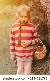 Upset Or Focused Eight Year Old Kid Girl Mushroom Picker Is Seek For And Picking Mushrooms In The Forest. Child Survivalists Gathers A Wild Fungus Harvest And Outdoor Foraging  In Nature. Flare