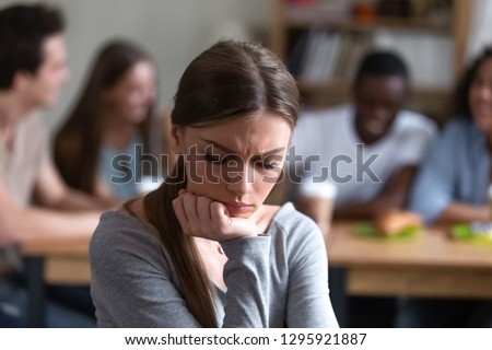 Upset frustrated young woman sitting alone in cafe, suffering from bullying, low self-esteem, discrimination, offended by friends, gossips, sad excluded female feeling outsider, bad friendship concept