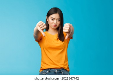 Upset Gloomy Asian Girl With Dark Haircut Frowning Sulking Sad, Disappointed, Show Thumbs-down Grimacing, Give Negative Opinion, Judging Bad Uninteresting Movie, Stand Blue Background