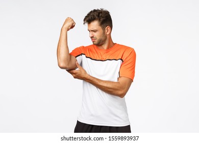 Upset Gloomy Handsome Young Man Feeling Weak As Raising Arm, Touching His Muscle And Frowning Sad, Grimacing Disappointed As Still Cant Reach Perfect Body Shape, Start Workout In Gym