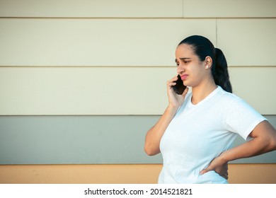 An Upset Hispanic Female Standing Next To A Wall And Talking On The Phone