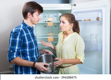 Upset Hungry Couple  Standing Near Empty Shelves Of Fridge