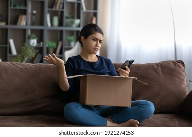 Upset Indian female buyer unbox package shopping online on smartphone confused with bad quality delivery service. Unhappy ethnic woman frustrated by wrong order buying on internet. Shipping concept.
