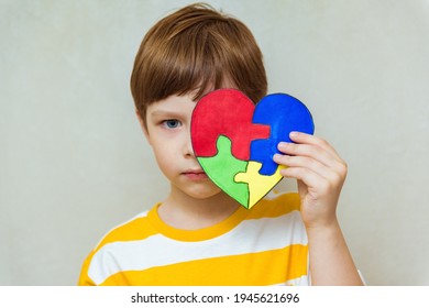 Upset Kid Boy Hands Holding Puzzle Heart On Gray Background. Child Mental Health Concept, World Autism Awareness Day