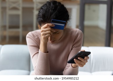 Upset latina female internet shopper sit on couch hold phone with opened web shop ebank page suffer of overspending money from card account. Frustrated young lady lost savings as scam operation result