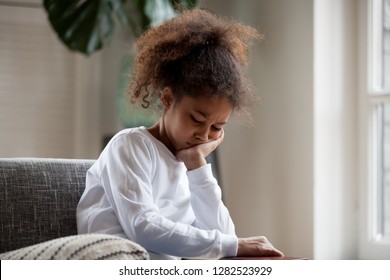 Upset little african american girl feels hurt sad bored sitting alone at home, depressed punished mixed race kid having psychological trauma, frustrated preschool black child thinking hiding problem