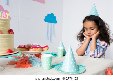 Upset Little African American Girl Sitting Alone At Birthday Table 