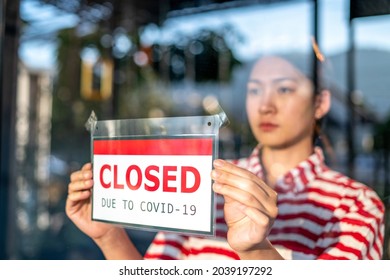 An upset Local small business owner woman or waitress is putting the sign for "sorry we closed" in front of the cafe, coffee shop, or retail store glass door cause lockdown quarantine due to covid-19. - Powered by Shutterstock