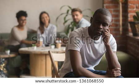 Upset lonely african american man suffering from bullying racial discrimination mocking racism social rejection sitting alone, sad depressed black outstand loser guy hurt excluded by diverse friends