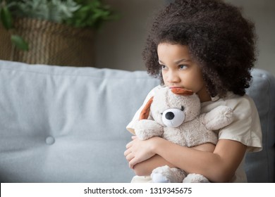 Upset Lonely Bullied Little African American Kid Girl Holding Teddy Bear Looking Away Feels Abandoned Abused, Sad Alone Preschool Mixed Race Child Orphan Hugging Stuffed Toy, Charity Adoption Concept