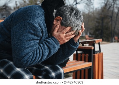 Upset lonely homeless elderly old Caucasian man with depression holds head in hands while sitting on a park bench in autumn - Powered by Shutterstock