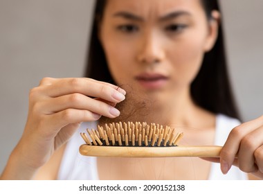 Upset long-haired millennial asian woman holding hairbrush, closeup shot. Young korean lady loosing hair, checking brush after combing hair. Hair loss, alopecia, symptoms and causes for women concept