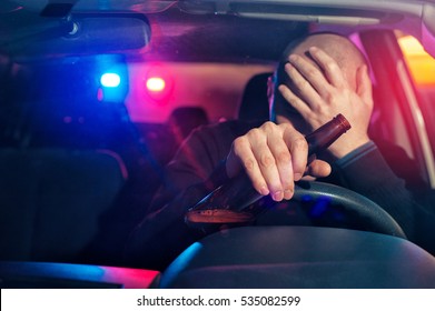 Upset male driver is caught driving under alcohol influence. Man covering his face from police car light. - Shutterstock ID 535082599