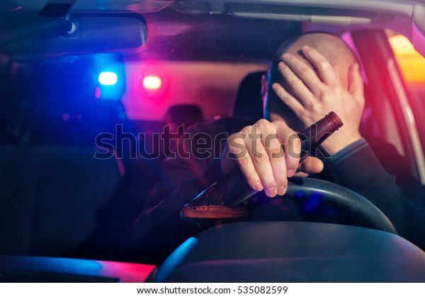 Upset male driver is
caught driving under alcohol influence. Man covering his face from
police car light.