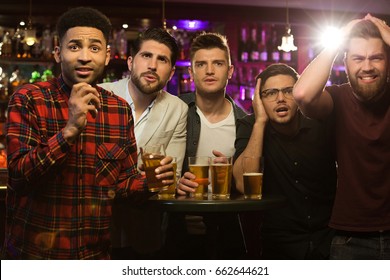 Upset Male Friends Watching Sport Game Or Football Match And Drinking Beer At Bar Or Pub