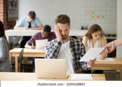 Upset Male Student Looking Sadly At Given Paper, Unsatisfied With Exam Mark. Intern Disappointed With Results Of Work Evaluation Examination. Concept Of Stress, Frustration And Failure