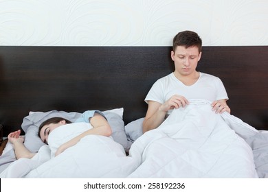 Upset man having problem with impotence sitting on bed while his girlfriend lying and sleeping. Sex problems in long relationship after sterss. Depressed husband looking at his penis