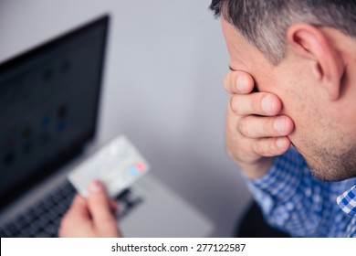 Upset man holding credit card with laptop on background