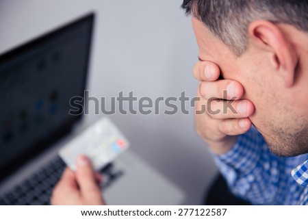 Upset man holding credit card with laptop on background
