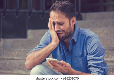 Upset Man Looking At His Mobile Phone Sitting On Steps Outdoors 