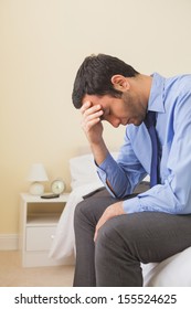 Upset Man Sitting Head In Hands On His Bed In A Bedroom At Home