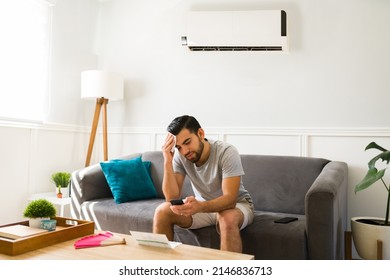Upset man sweating during a heat wave in the summer while at home with a cold ac unit - Shutterstock ID 2146836713