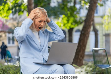 Upset mature businesswoman reading bad news on laptop sitting on bench on city street. Frustrated female employer in formal suit received unpleasant notification, worriedly looks at negative message. - Powered by Shutterstock