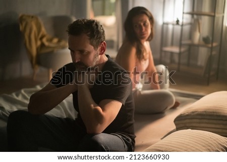 Upset mature man with his wife in bed hehind him, relationship problems concept.