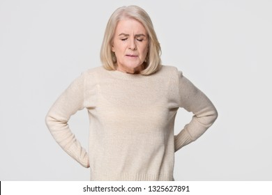 Upset mature old woman touching back feel hurt osteoarthritis kidney spine ache massage sore muscles, sad senior mid aged lady suffer from lower lumbar pain isolated on white grey studio background