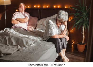 Upset Mature Woman Sitting In Bed Near Her Husband At Home. Sad Senior Woman And Man  In A Quarrel. Relationship Problems
